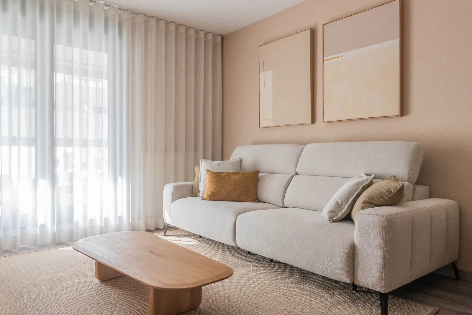 Salón con sofá lino, mesa de roble orgánica, cuadros abstractos y cortinas translúcidas